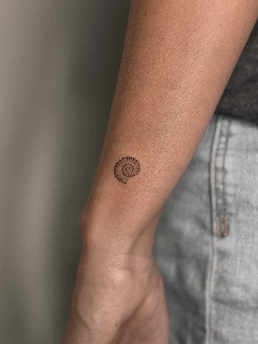 Tatuaje de línea fina: amonita en la muñeca